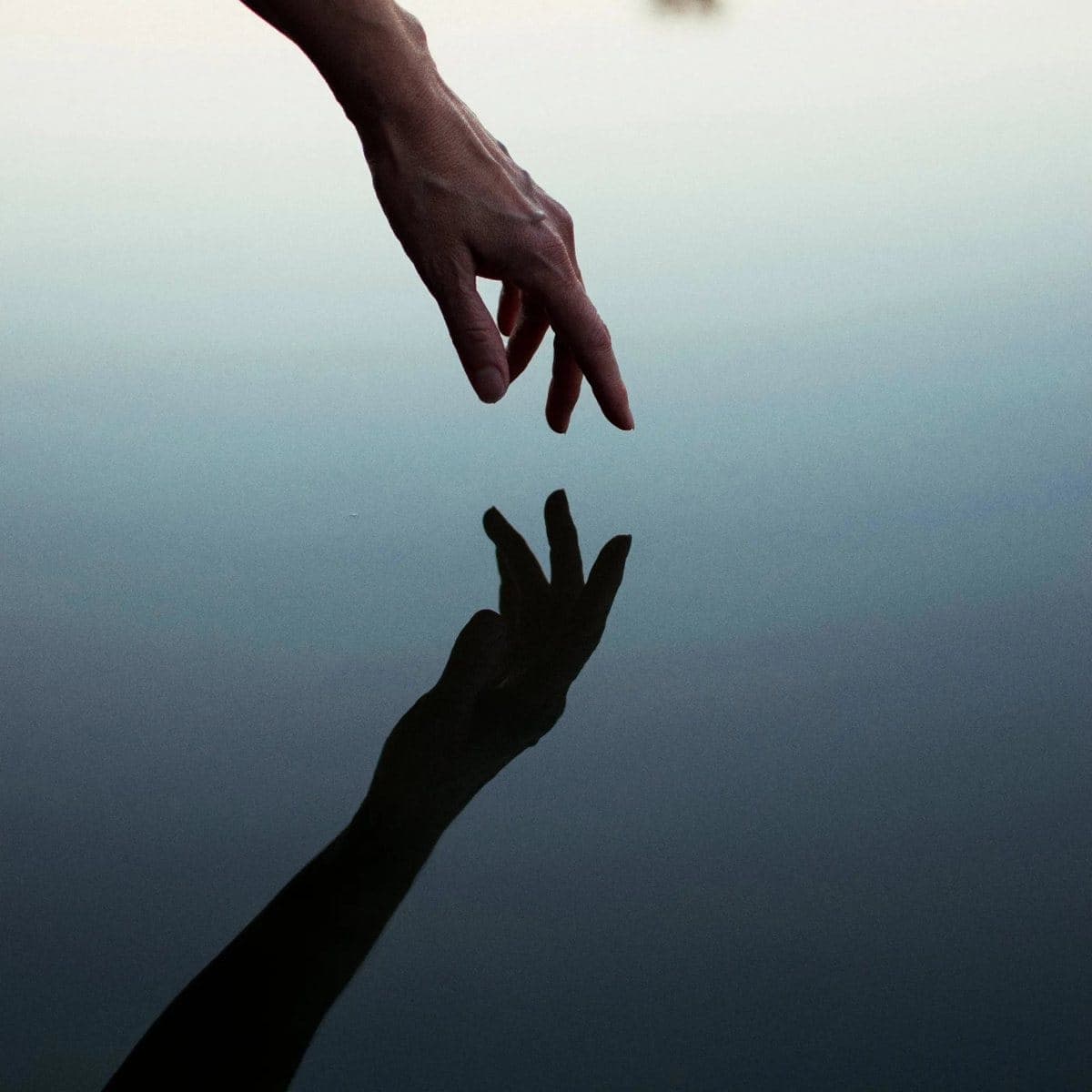 Una mano que se encuentra con su reflejo en el agua